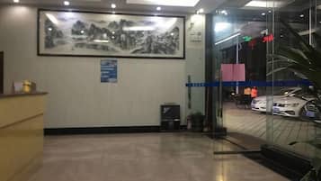 A reception area with a desk, a framed artwork on the wall, a glass door leading to a car display, and a blue directional sign.