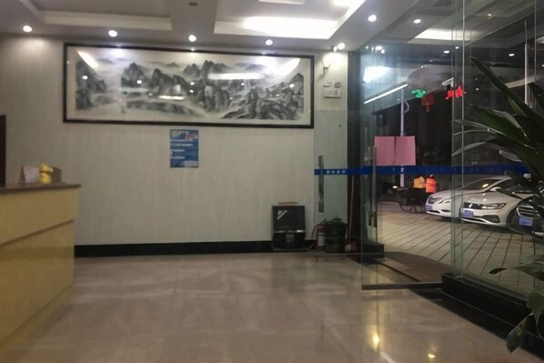 A reception area with a desk, a framed artwork on the wall, a glass door leading to a car display, and a blue directional sign. - Tengyun Hotel (Huaiji)