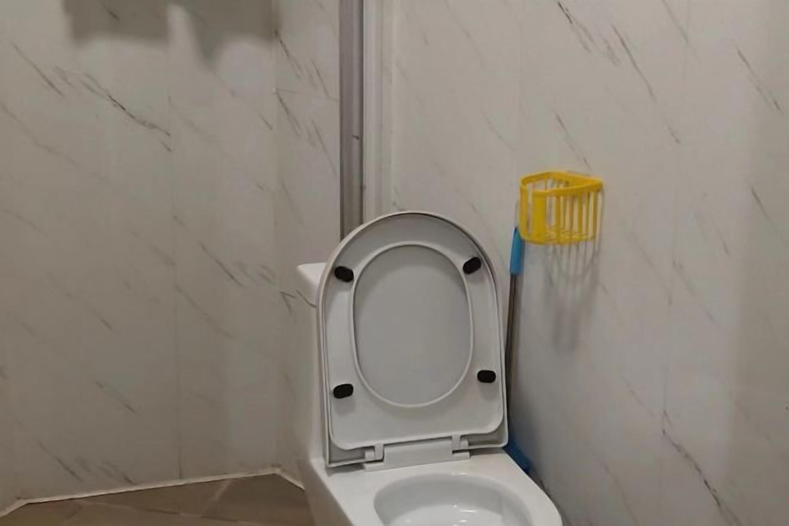 Un baño con un inodoro blanco, un soporte amarillo para cepillos de limpieza y una pared de mármol.