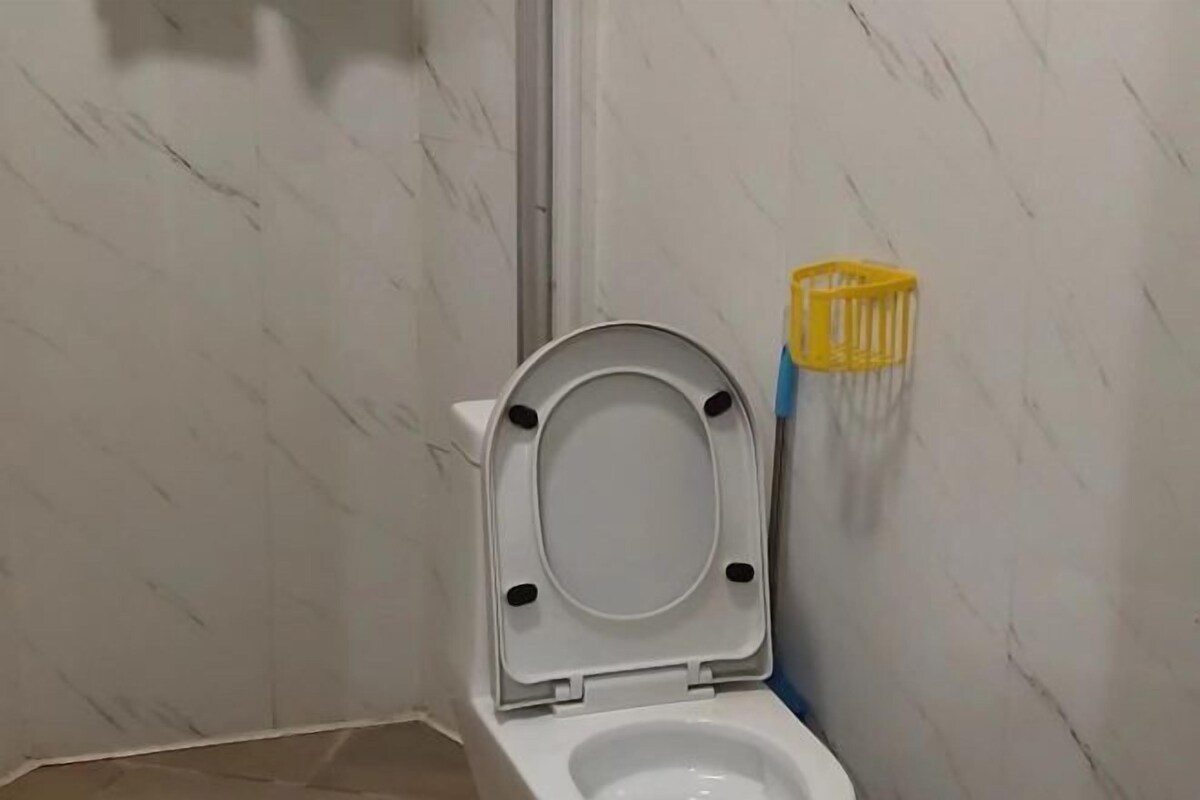 A bathroom with a white toilet, a yellow cleaning brush holder, and a marble wall.