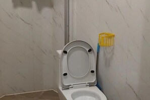 A bathroom with a white toilet, a yellow cleaning brush holder, and a marble wall. - Tengyun Hotel (Huaiji)