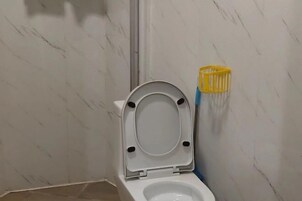 Un baño con un inodoro blanco, un soporte amarillo para cepillos de limpieza y una pared de mármol.