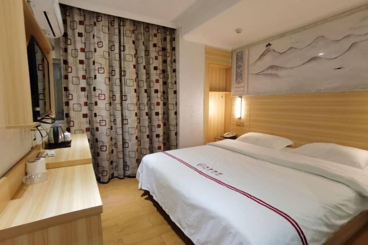 Una habitación de hotel con cama, un escritorio de madera, un espejo, cortina estampada y una obra de arte colgada en la pared.