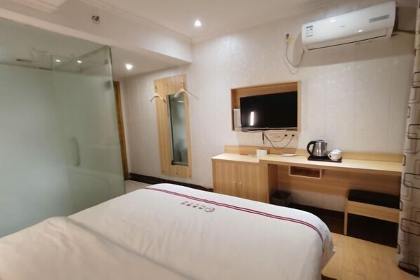 A hotel room with a bed, a desk with a flat-screen TV, a coffee maker, and an air conditioner.