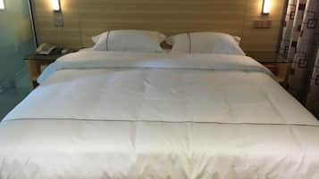 Uma cama bem arrumada com lençóis brancos, uma mesa de cabeceira com abajur e um telefone.