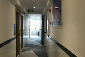A hallway with a carpeted floor, doors on both sides, and a sign indicating an exit.