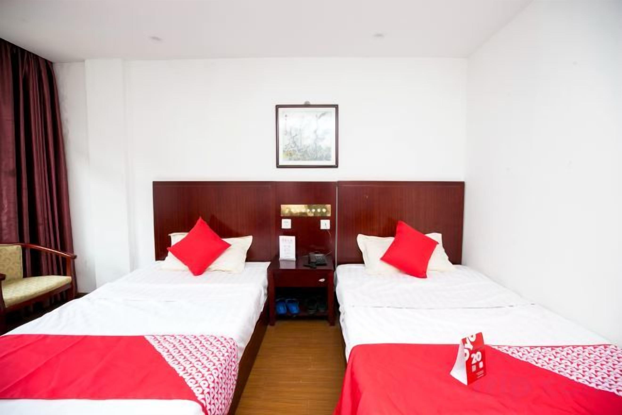 A hotel room with two beds, each with red bedding, a wooden headboard, and a small table between the beds.