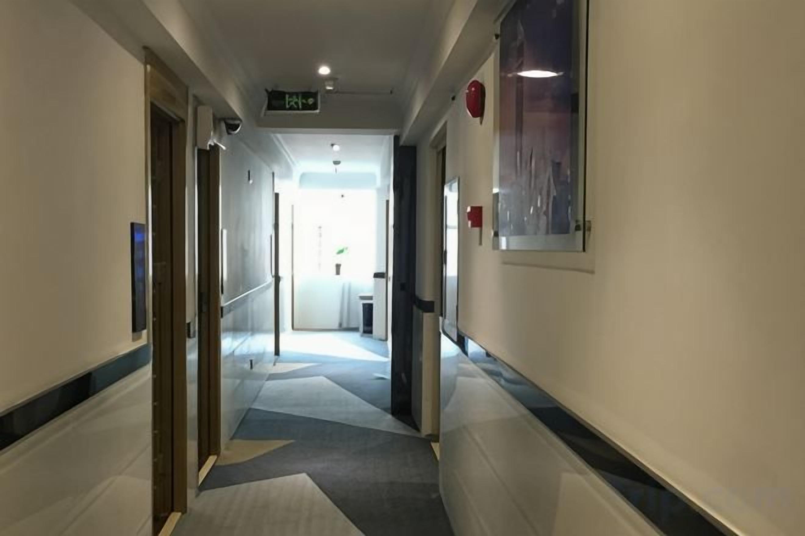 Un couloir d’hôtel avec un sol recouvert de moquette, des portes des deux côtés et un panneau indiquant la sortie.