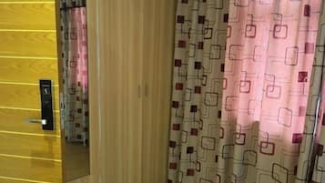 Quarto de hotel com chão de madeira, um espelho, cortina estampada e uma porta com puxador.