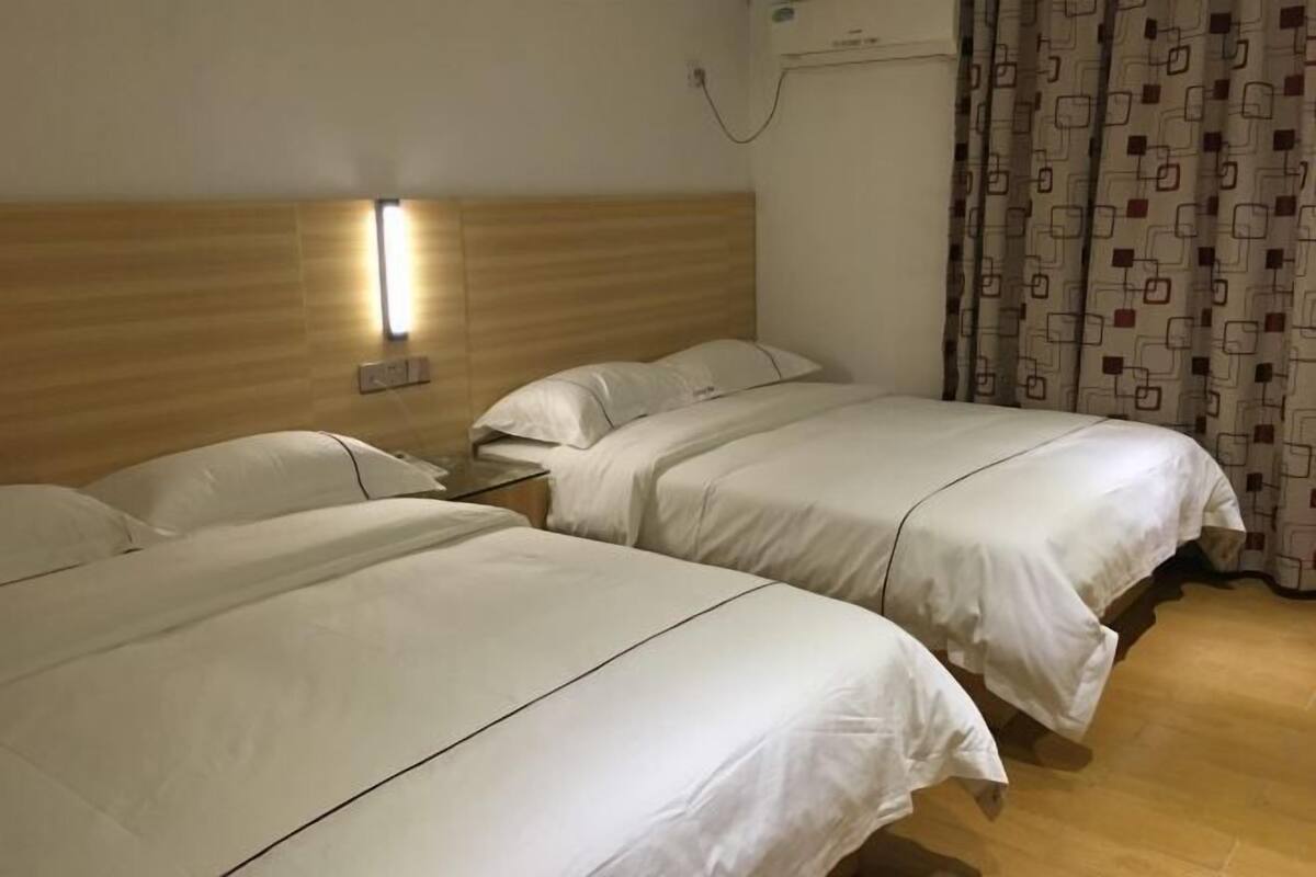 Habitación de hotel con dos camas individuales, cabecero de madera, mesita de noche y aire acondicionado instalado en la pared.