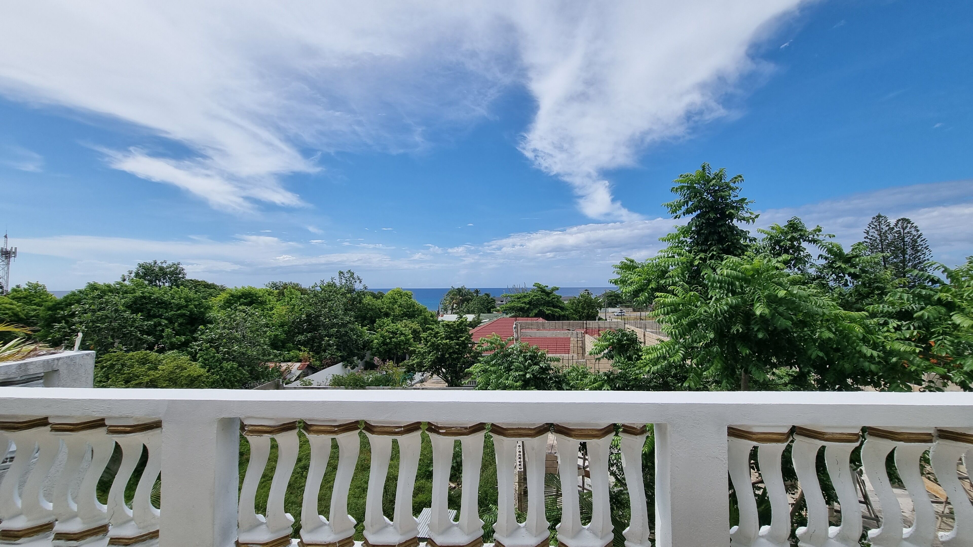 A balcony with a white balustrade overlooking a coastal area with trees and buildings.