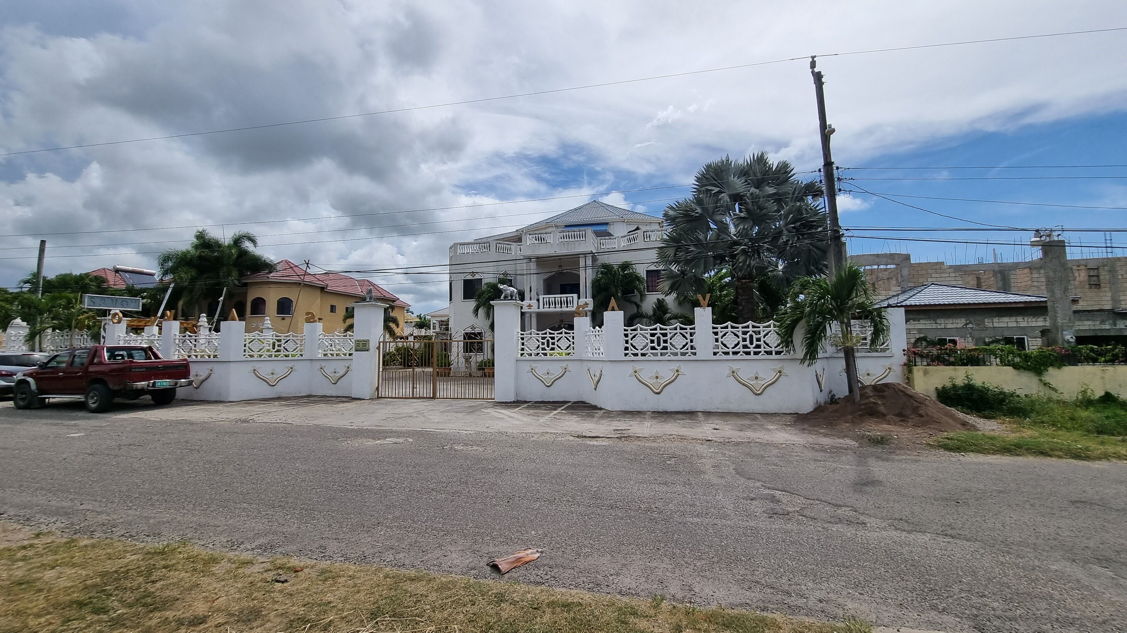 Zona residencial cerrada con una casa grande, techo rojo y valla blanca.