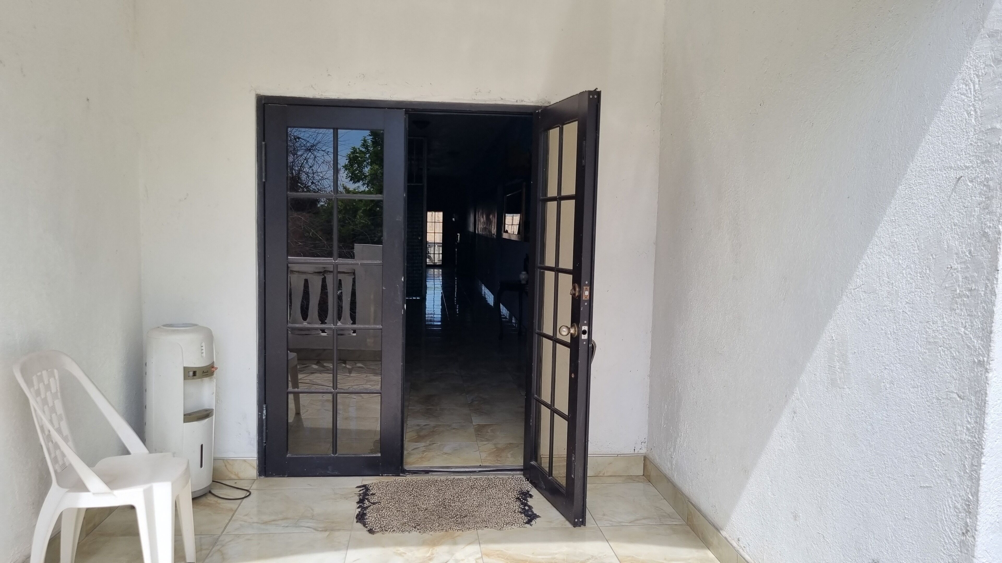 Una habitación con puerta de vidrio corredera que da a un balcón, una silla blanca y un pequeño calentador en el suelo.