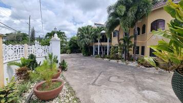 A paved driveway leading to a building with a white fence and potted plants.