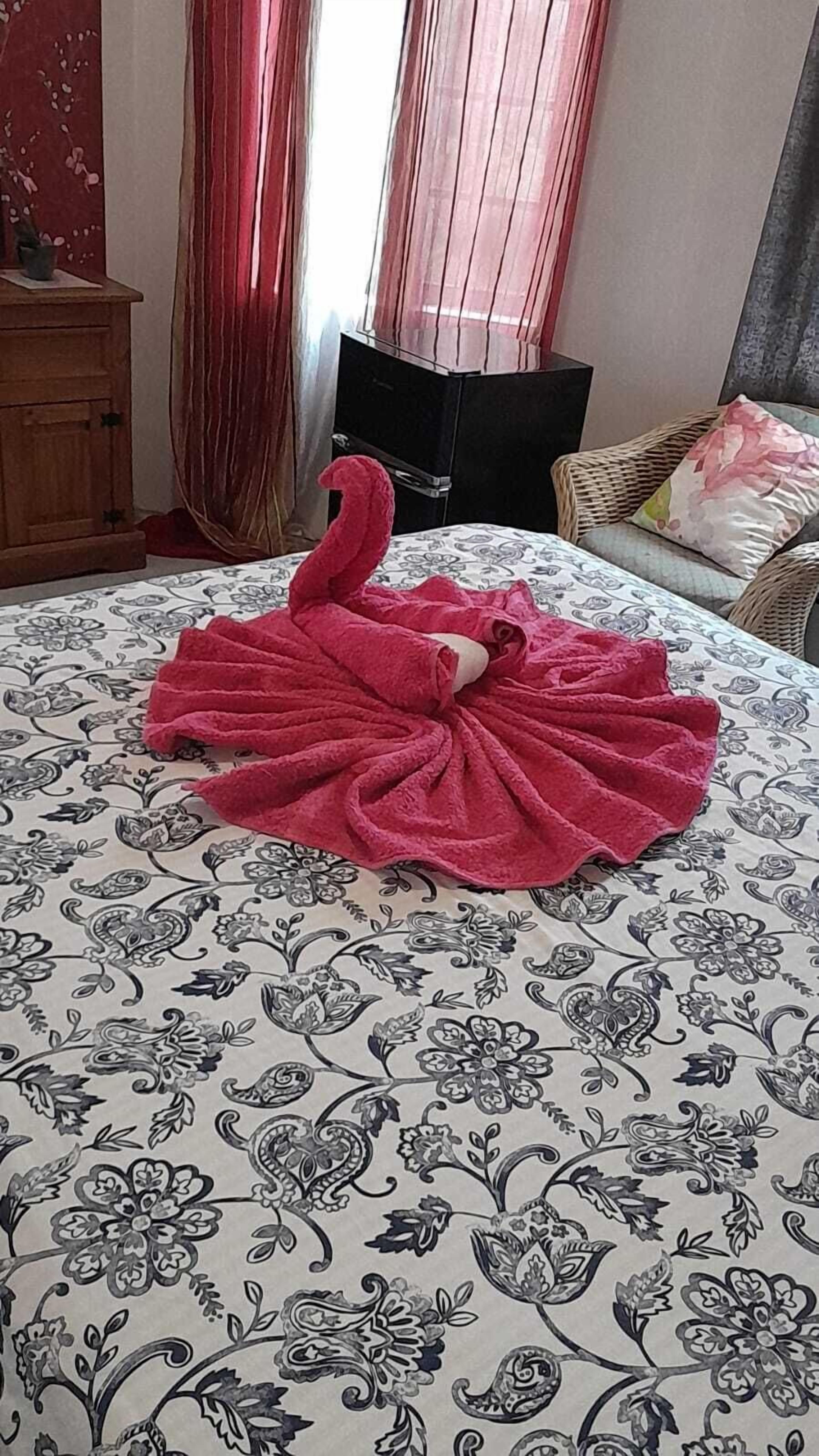 A bed with a floral-patterned bedspread, a red towel arranged in a swan shape, a wooden dresser, and a black chair.