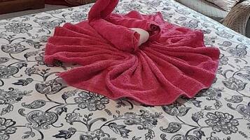 A bed with a floral-patterned bedspread, a red towel arranged in a swan shape, a wooden dresser, and a black chair.