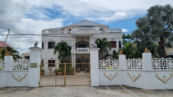 A large, white, two-story house with a gated entrance, decorative columns, and a statue of an elephant on the roof. - Little Savoy Guest House (Runaway Bay)