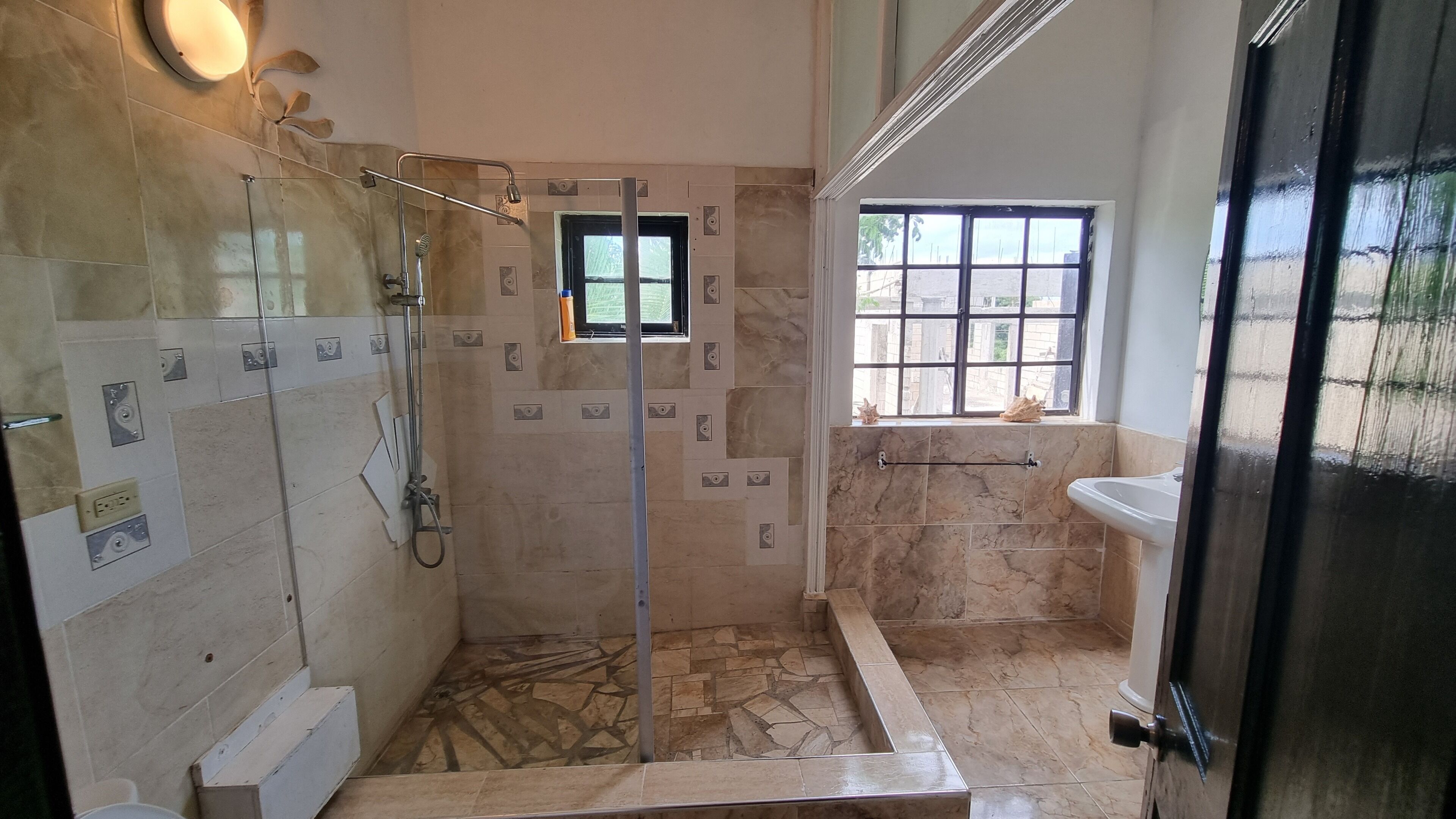 A shower area with a glass door, tiled walls, a window, and a sink.