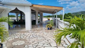 A covered outdoor area with a tiled floor, white pillars, and potted plants.