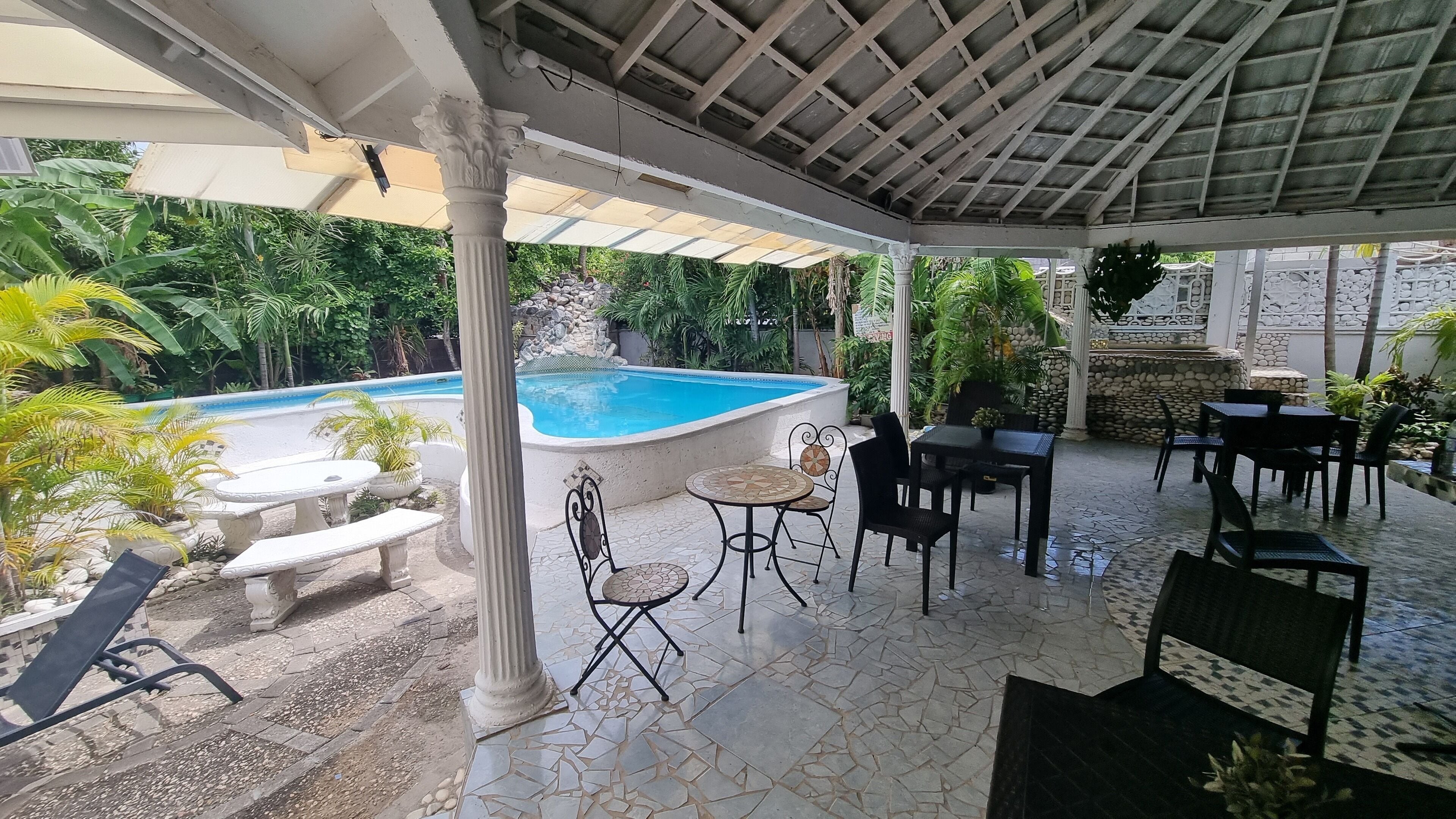 A covered outdoor area with a pool, seating, and potted plants.