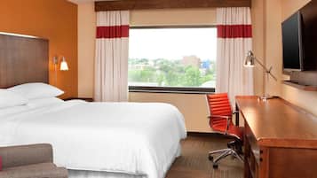 Ein Hotelzimmer mit einem großen Bett, einem Schreibtisch mit Stuhl, einem Fernseher und einem Fenster mit Vorhängen.