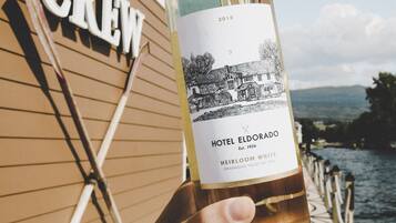 A bottle of Hotel Eldorado Heirloom White wine held by a person, with a wooden boat deck and a 'CREW' sign in the background.