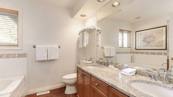 A bathroom with a double sink, toilet, and bathtub. There are towels hanging on the wall and a framed picture above the mirror.