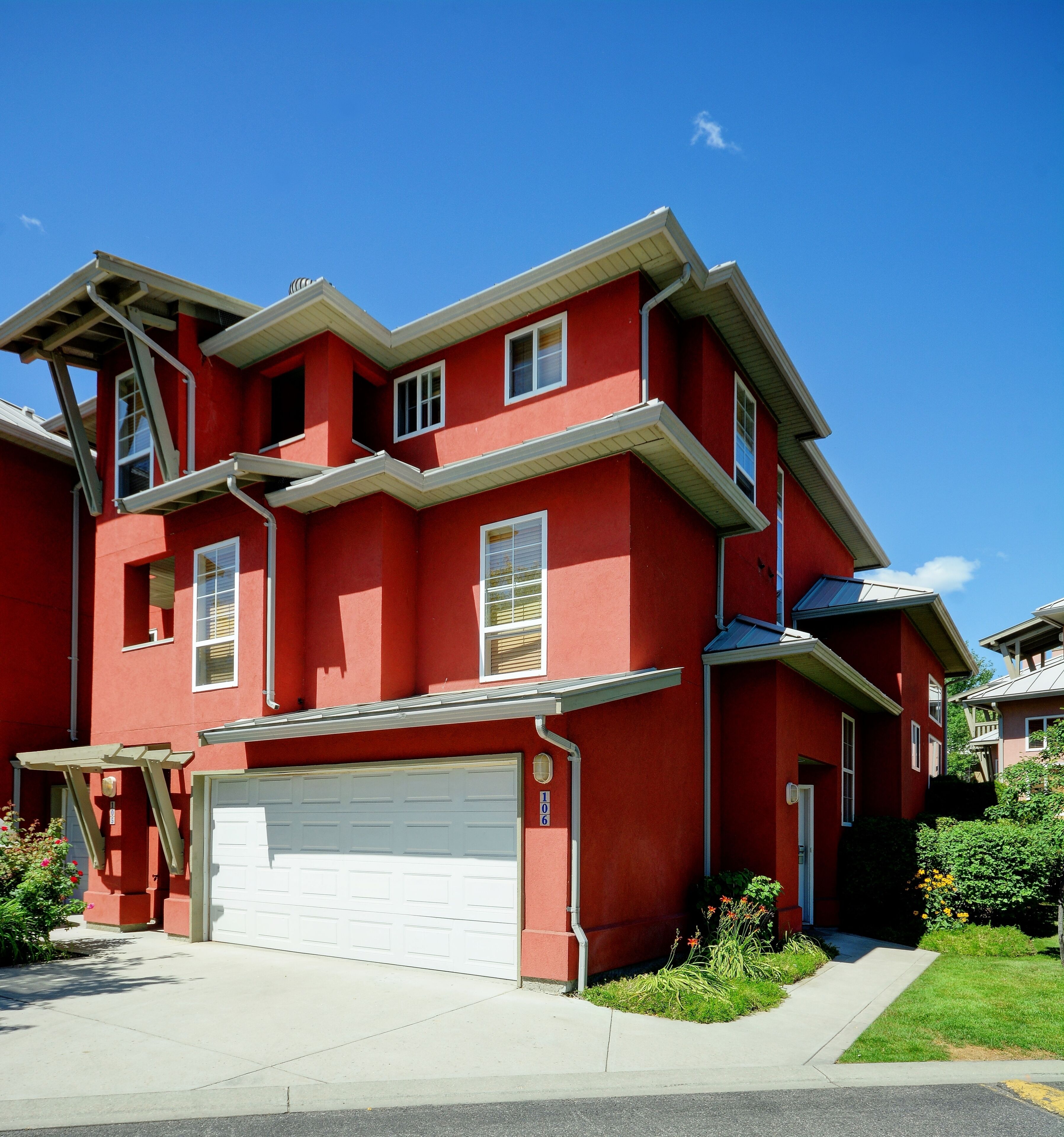 A two-story red house with a white garage door, a small porch, and a clear blue sky.