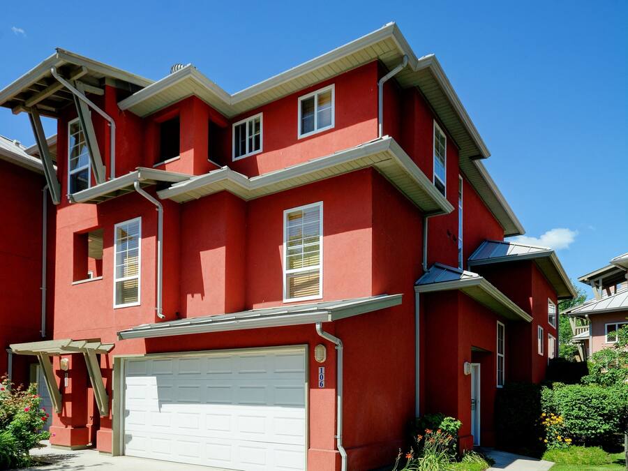 A two-story red house with a white garage door, a small porch, and a clear blue sky.