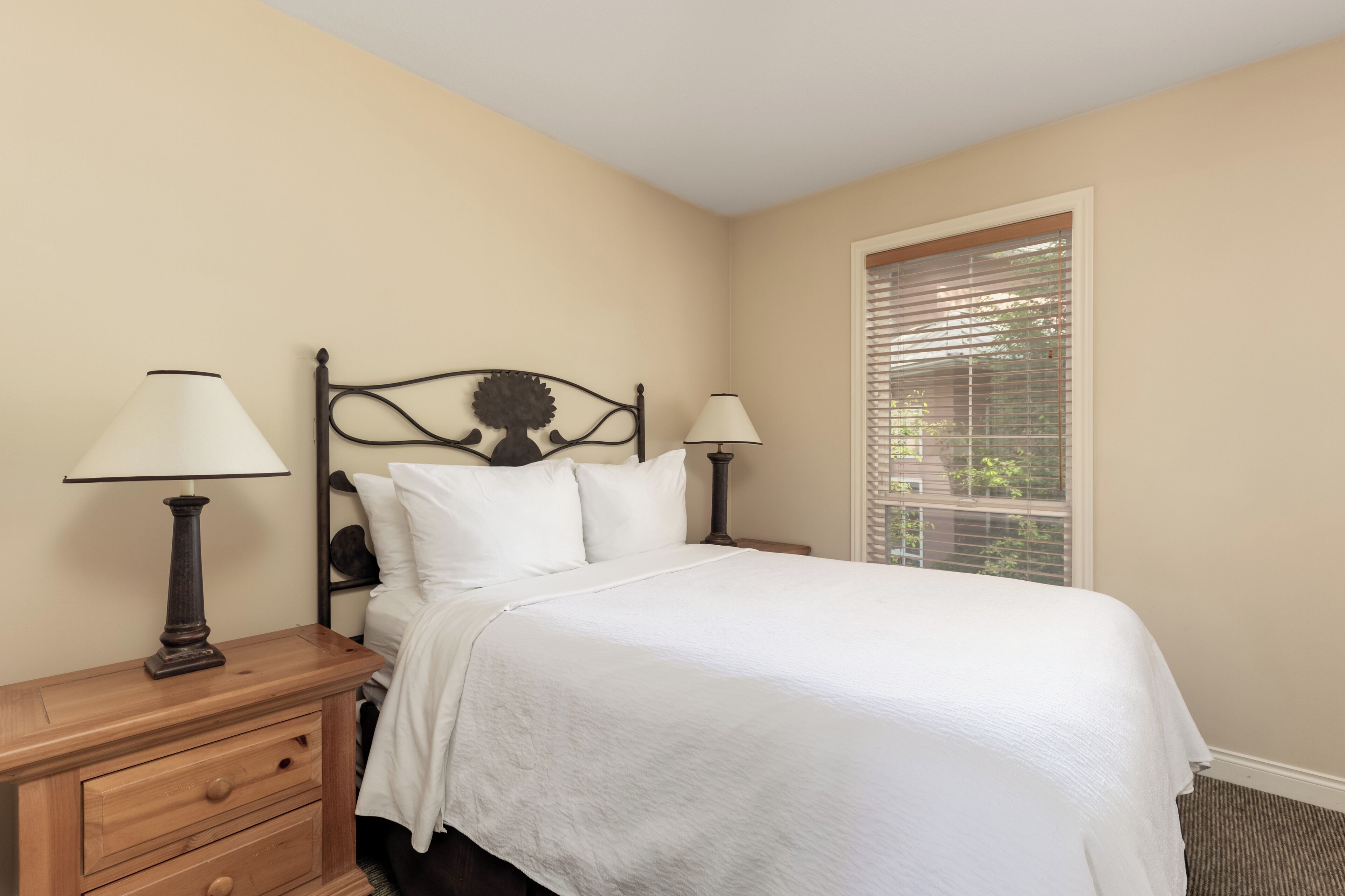 A neatly made bed with white linens, two bedside lamps, and a wooden nightstand with drawers.