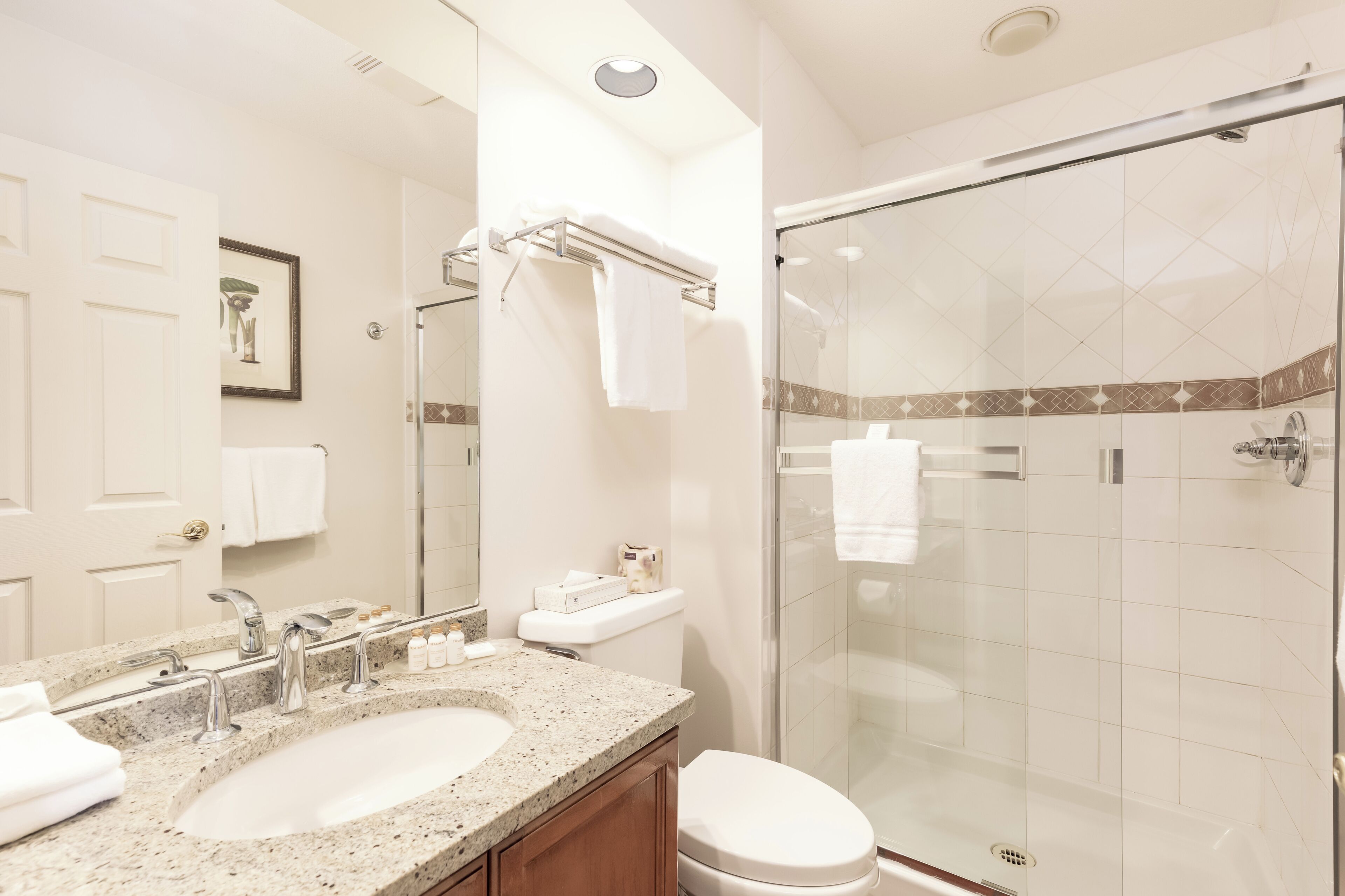 A modern bathroom with a granite sink, a toilet, and a glass-enclosed shower.