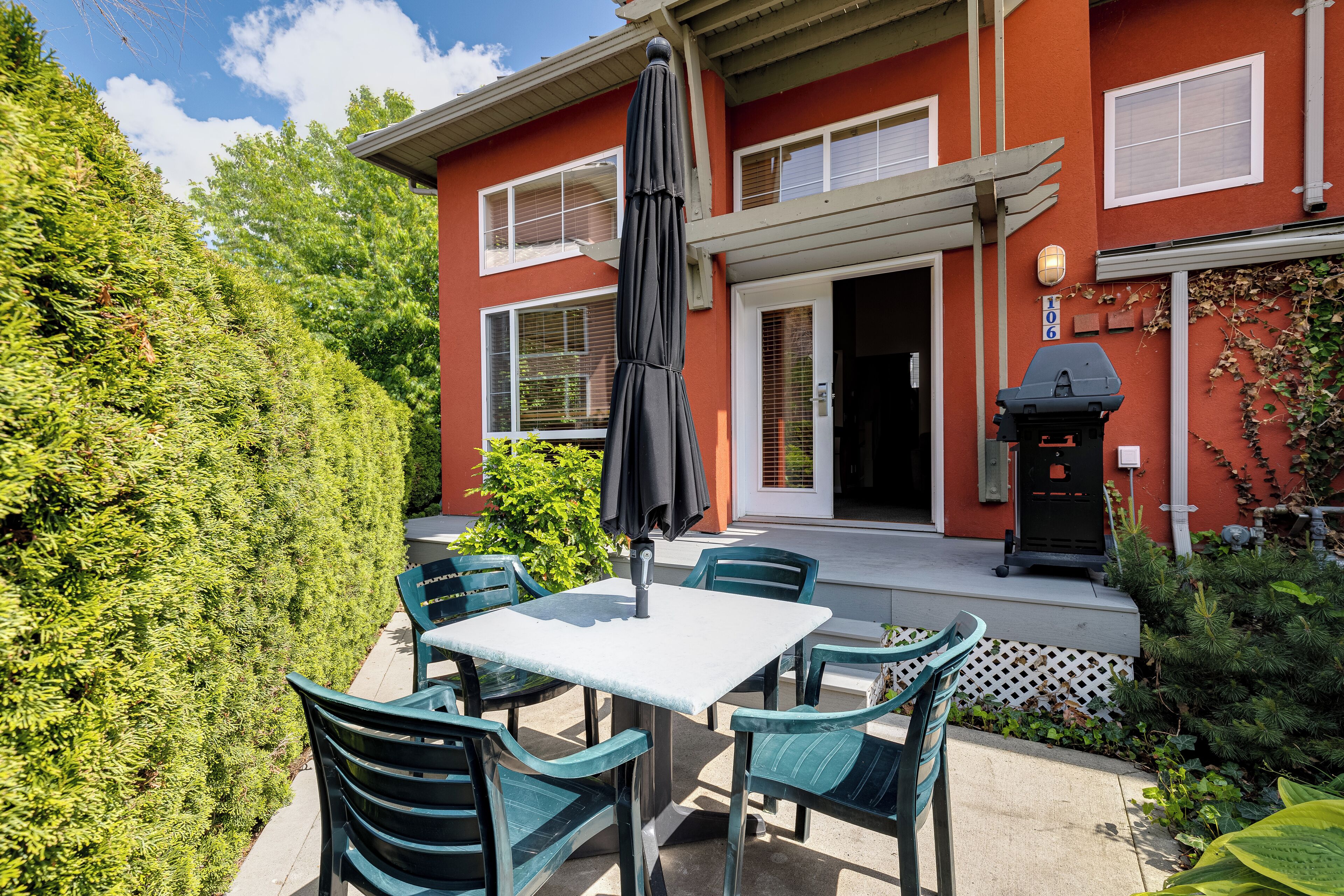 A patio with a table and chairs, a grill, and a house with a red exterior.
