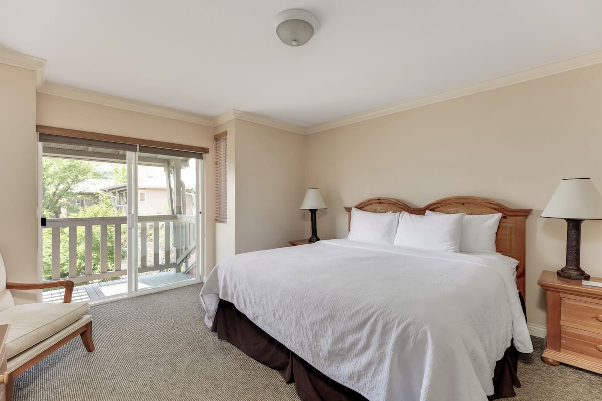 A hotel room with a large bed, two bedside tables with lamps, a chair, and a balcony with a view.