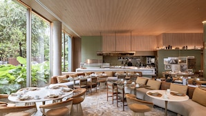 A modern restaurant with large windows, a kitchen area, and a variety of seating options including tables and sofas.