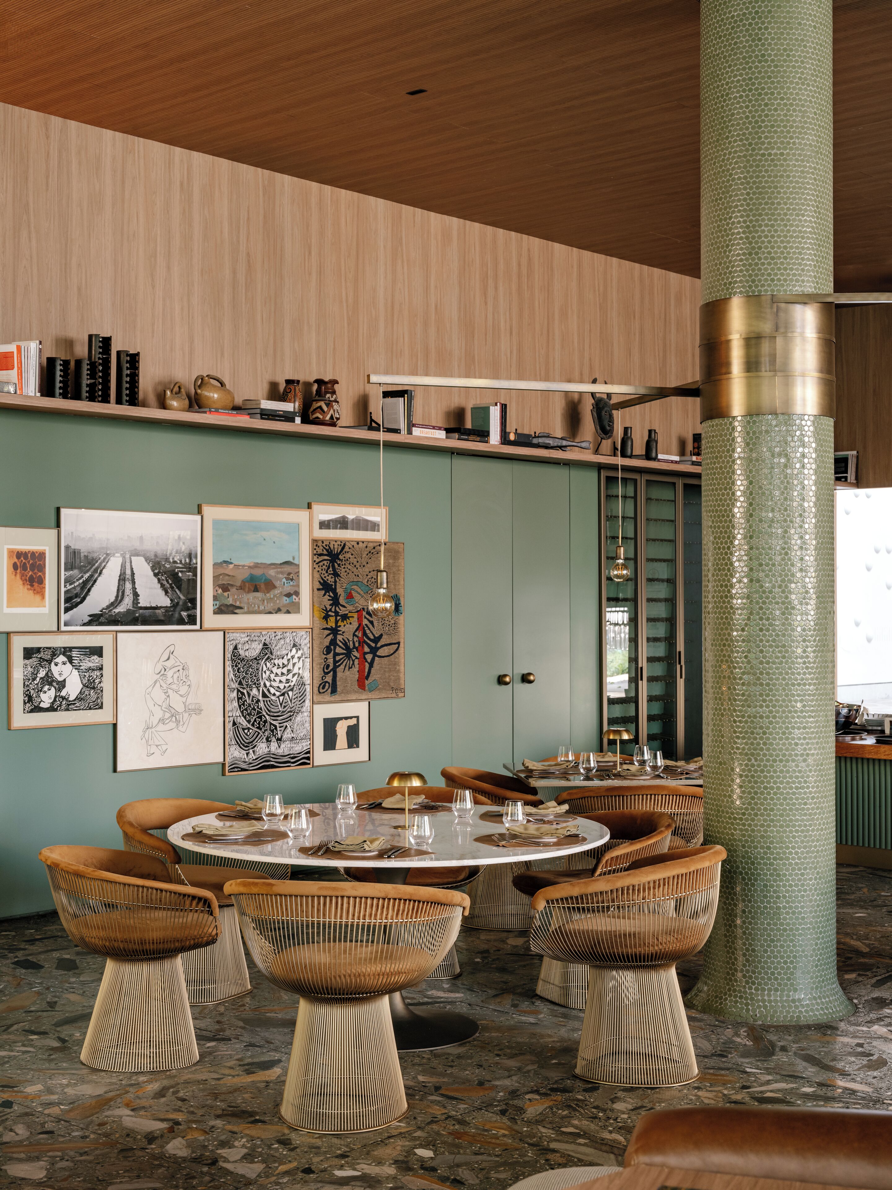 Un espace repas avec des tables rondes, des chaises en osier et des œuvres d’art accrochées aux murs.