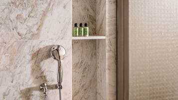 A bathroom with a shower, a handheld showerhead, and a shelf with toiletries.