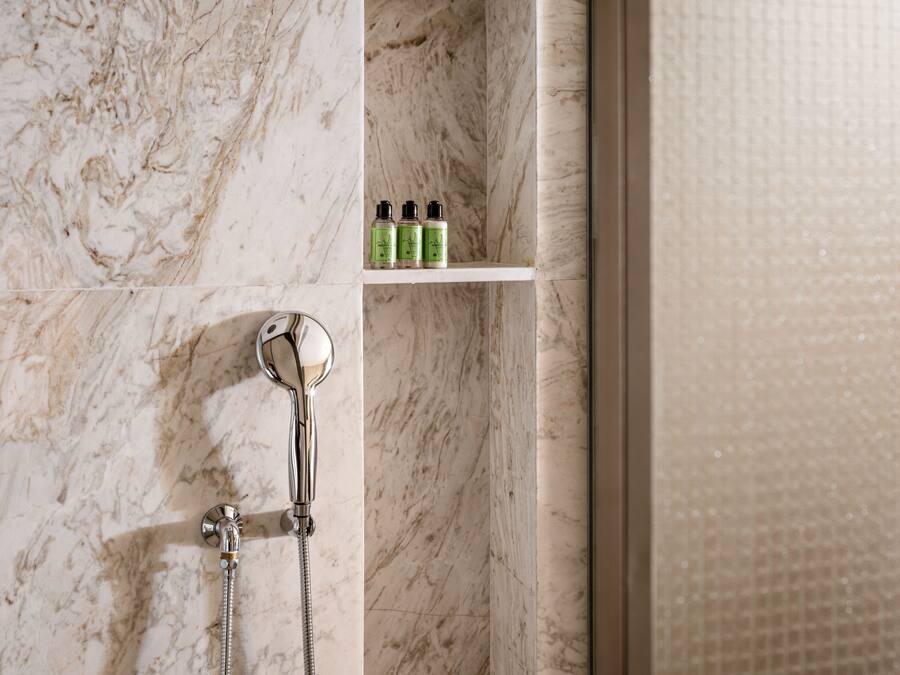 A bathroom with a shower, a handheld showerhead, and a shelf with toiletries.