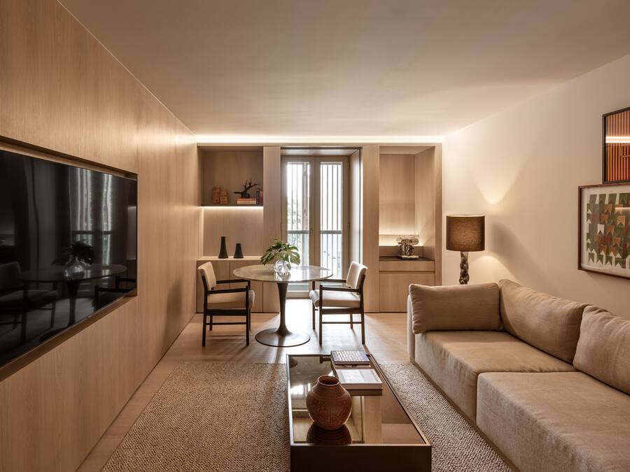 A modern living room with a flat-screen TV, a round dining table with chairs, a sofa, and a coffee table with a vase.