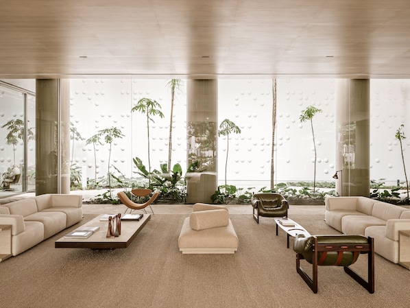 A spacious living room with large windows, a beige sofa, a coffee table, and a leather armchair.
