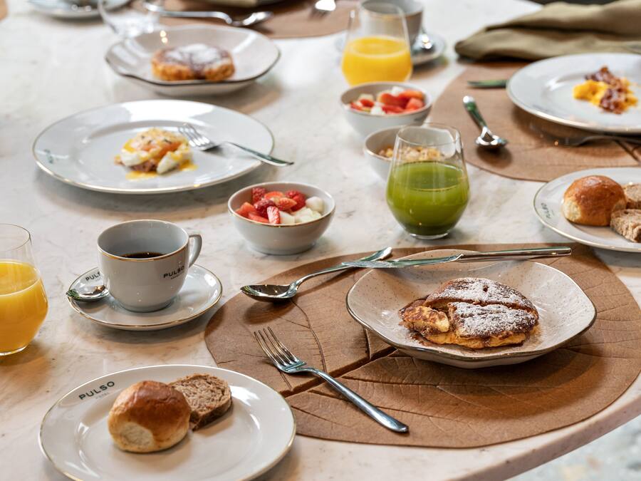Ein Frühstückstisch mit Tellern voller Speisen, einer Kaffeetasse und einem Glas Orangensaft.