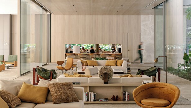A modern living room with a sofa, coffee table, and a television. There is a bar area with chairs and a large window.