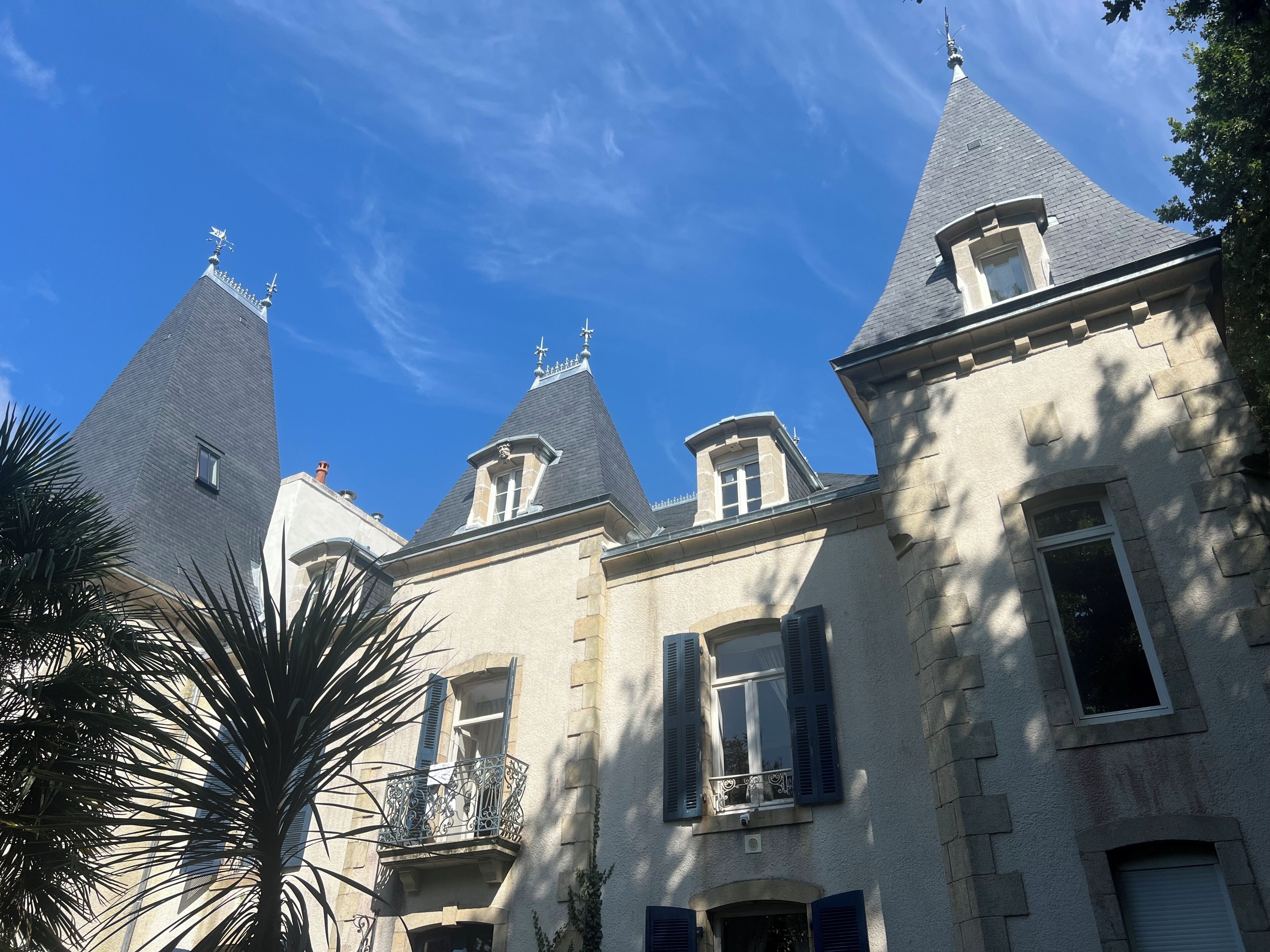 Un bâtiment historique doté de plusieurs tours, d’un balcon orné de ferronnerie et d’une façade en pierre.