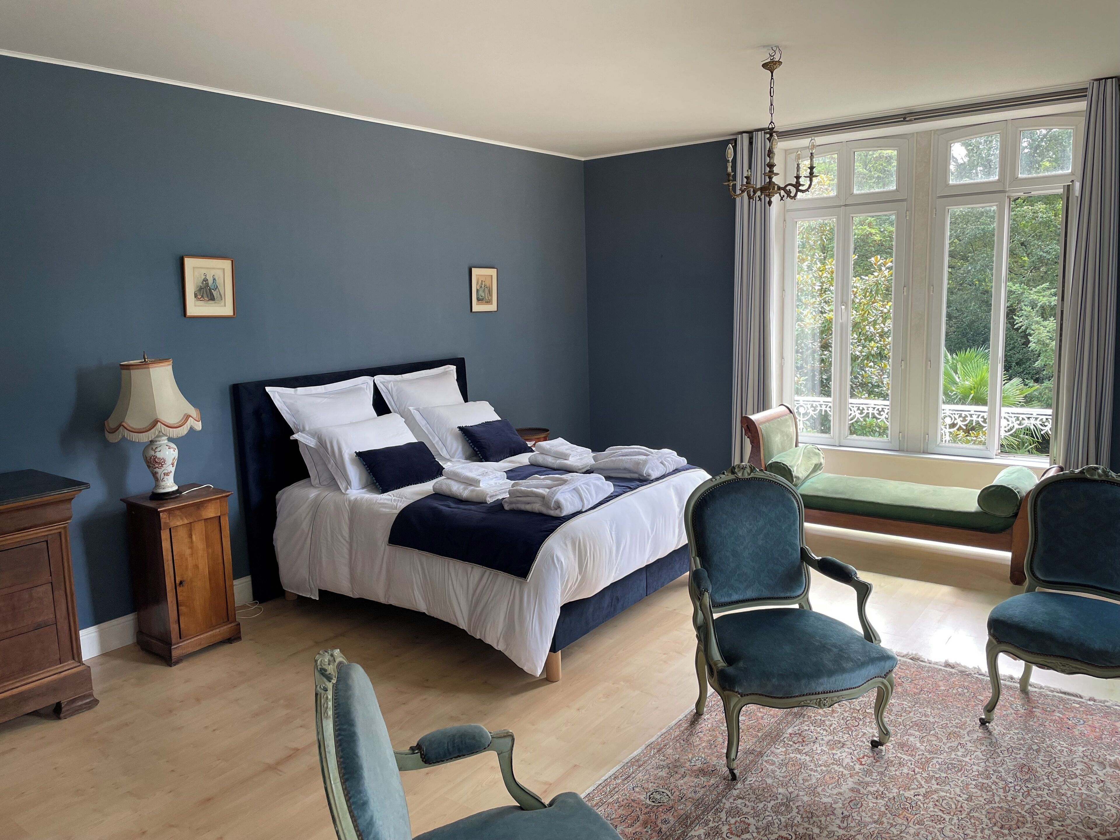 Une chambre à coucher comprenant un lit, deux chaises, une table de chevet, une lampe et une fenêtre donnant sur un paysage verdoyant.