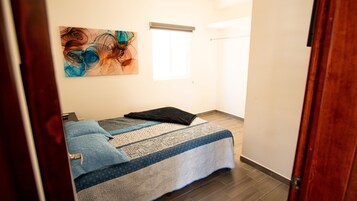 A bedroom with a bed, a window, and a painting on the wall.