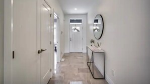 A hallway with white doors, a mirror, and a console table with decorative items. - Luxurious 3BR, King Bed, Ensuite. Perfect Stay! (Windsor)