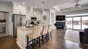 A modern kitchen with white cabinets, stainless steel appliances, and a central island with bar stools. - Luxurious 3BR, King Bed, Ensuite. Perfect Stay! (Windsor)