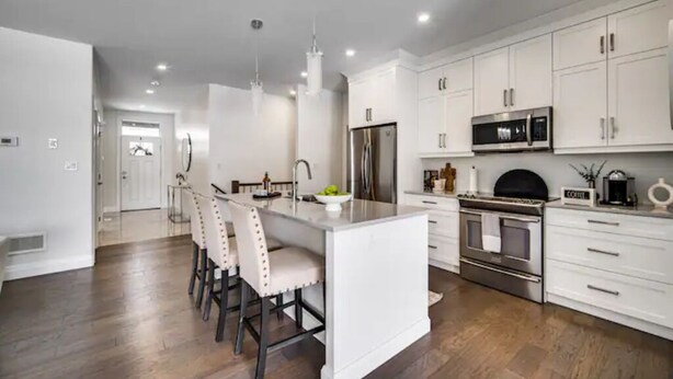A modern kitchen with white cabinetry, stainless steel appliances, and a central island with bar stools. - Luxurious 3BR, King Bed, Ensuite. Perfect Stay! (Windsor)