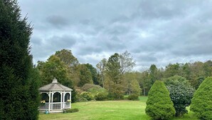 Ein Pavillon in einem üppigen Garten mit ordentlich geschnittenen Hecken und Bäumen im Hintergrund.