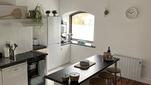 Una cucina moderna con mobili bianchi, un piano di lavoro nero e pavimento in legno. Si vede una finestra che lascia entrare luce naturale e un orologio appeso al muro.