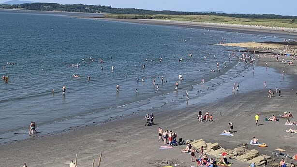 Una spiaggia con persone che nuotano e passeggiano sulla riva.